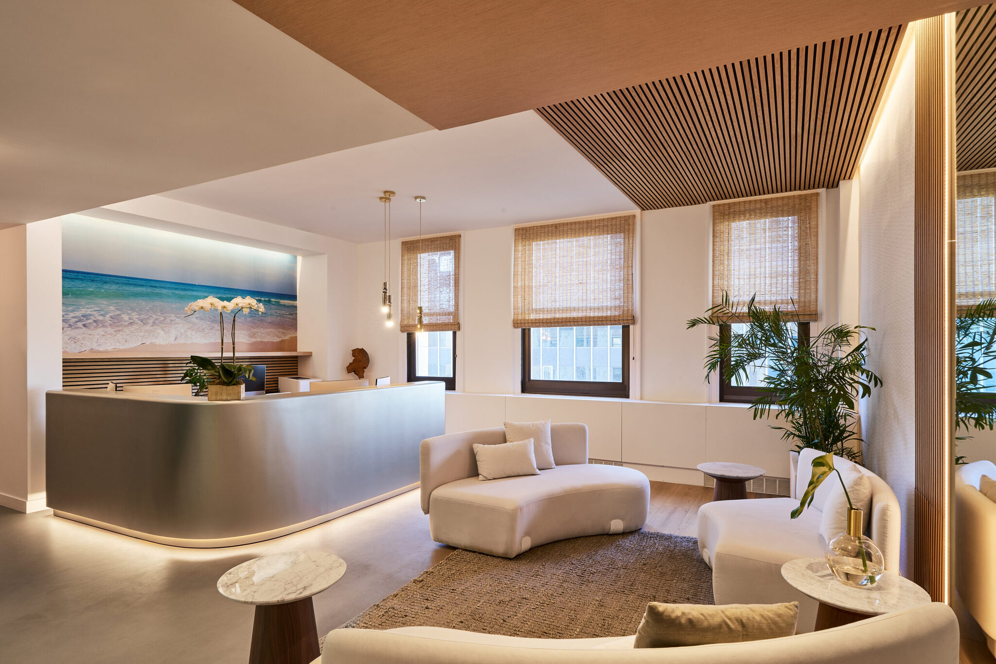 Reception lounge with a curved sofa, slatted wood ceiling and a large seascape photograph