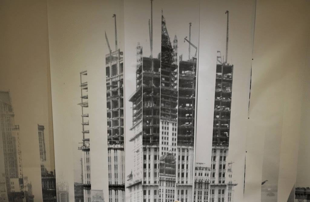 Archival photograph of the Woolworth Building under construction, its steel frame rising above neighbouring rooftops