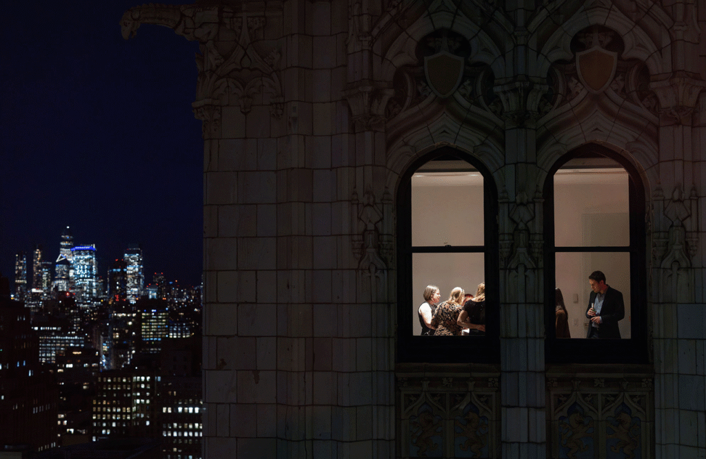 Guests gathered behind the Woolworth Building's lit Gothic windows at night, with the Manhattan skyline beyond