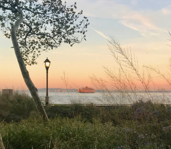 Sunset over New York Harbor from The Battery, with a ferry passing beyond the seawall