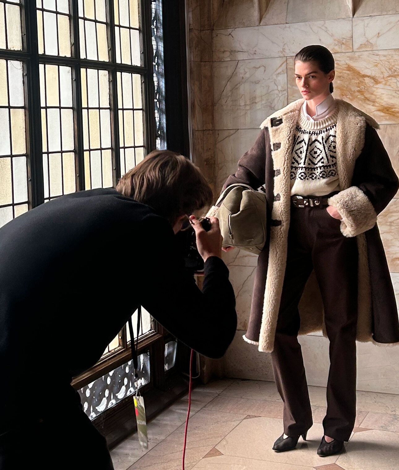 Photographer shooting a model in a shearling coat against the building's marble and leaded glass