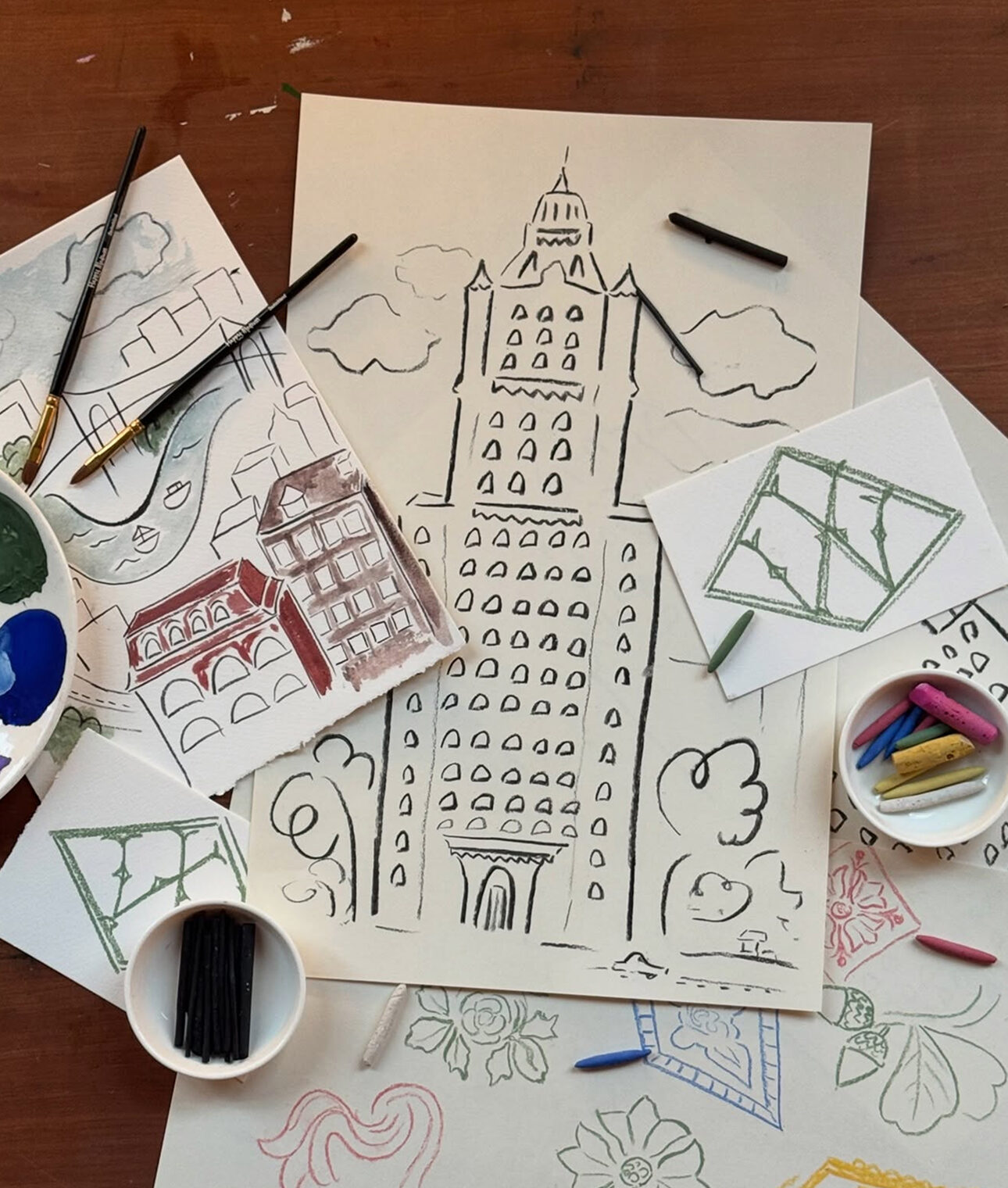 Drawings of the Woolworth Building on a worktable surrounded by brushes, pastels and paint