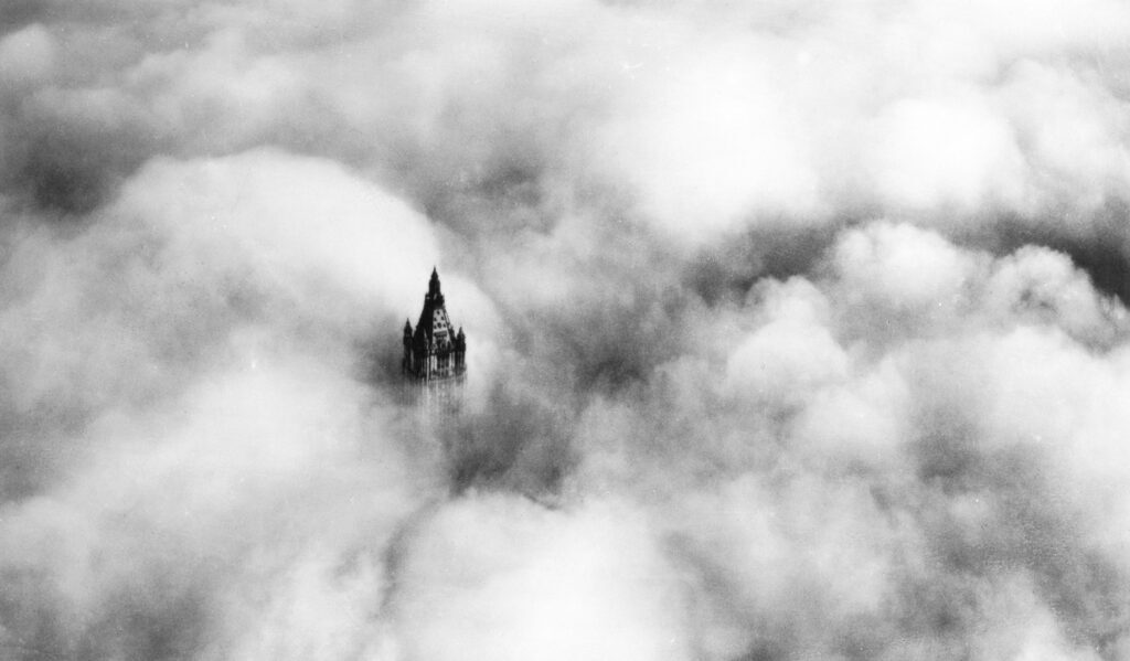 Woolworth Building tower rising through clouds in black and white