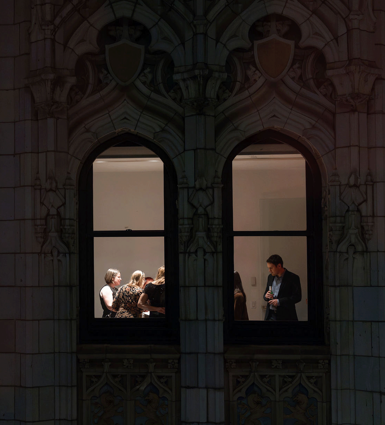 Guests visible through a Gothic window at night