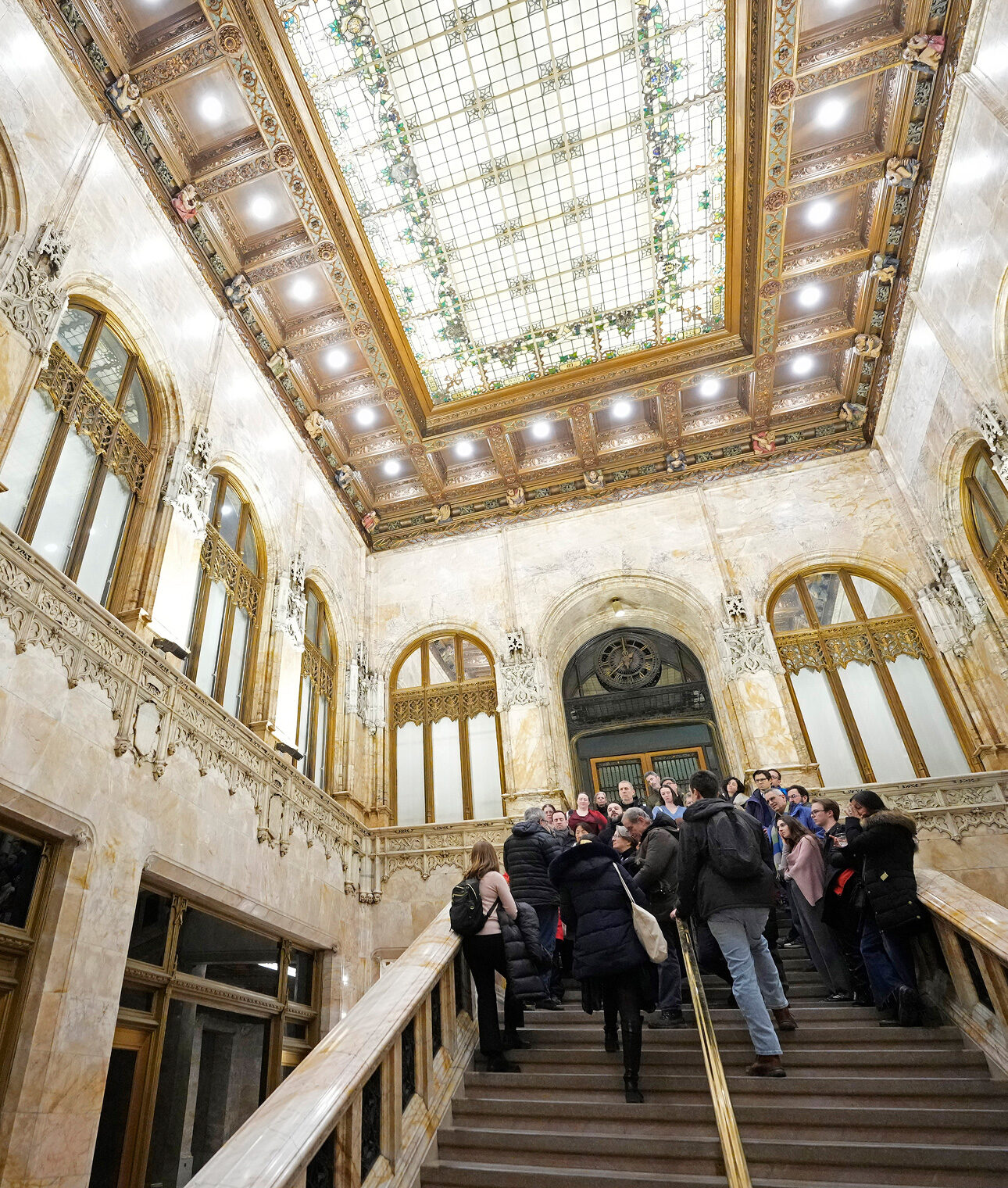 Tour group climbing the marble staircase beneath the Woolworth lobby's gilded mosaic ceiling