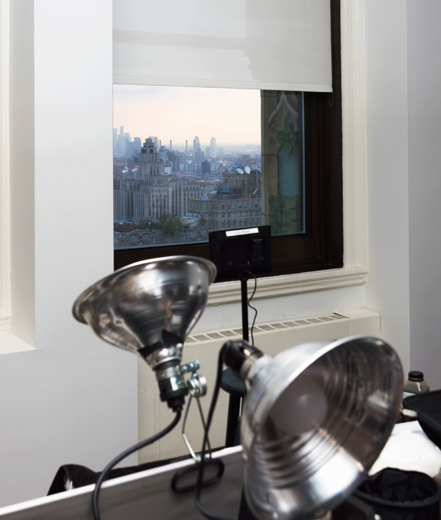 Studio lights beside a Woolworth Building window overlooking the Manhattan skyline